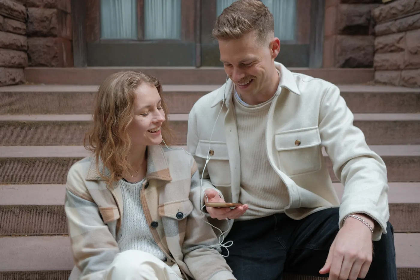 Couple sharing earphones on brownstone steps