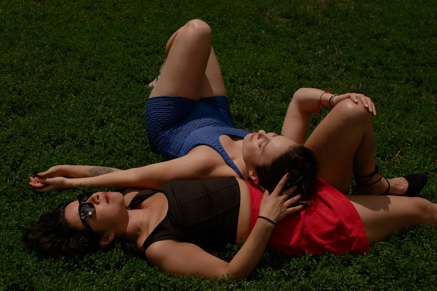 Two women resting head to shoulder in the grass, eyes closed in the sun