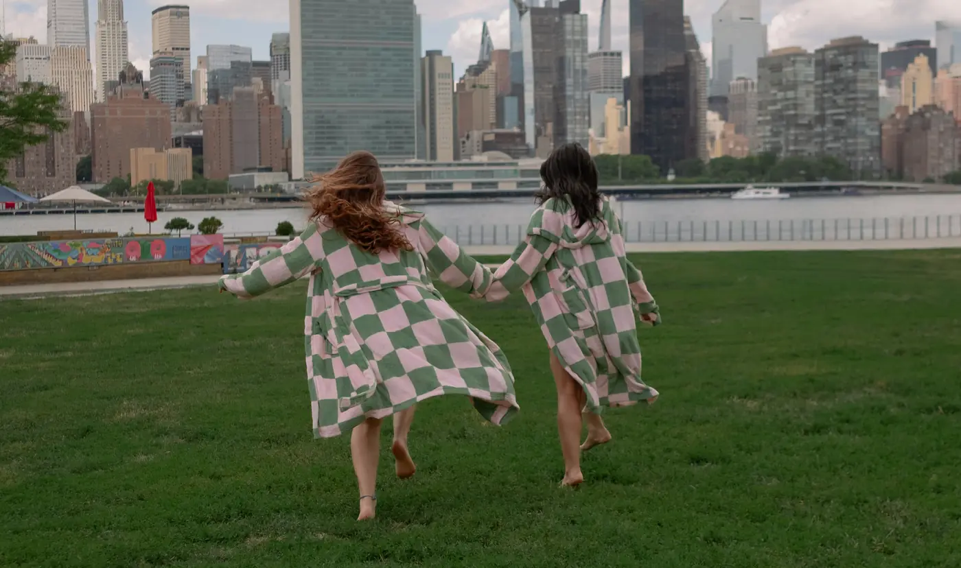 Two friends in checkered robes running hand in hand across the lawn