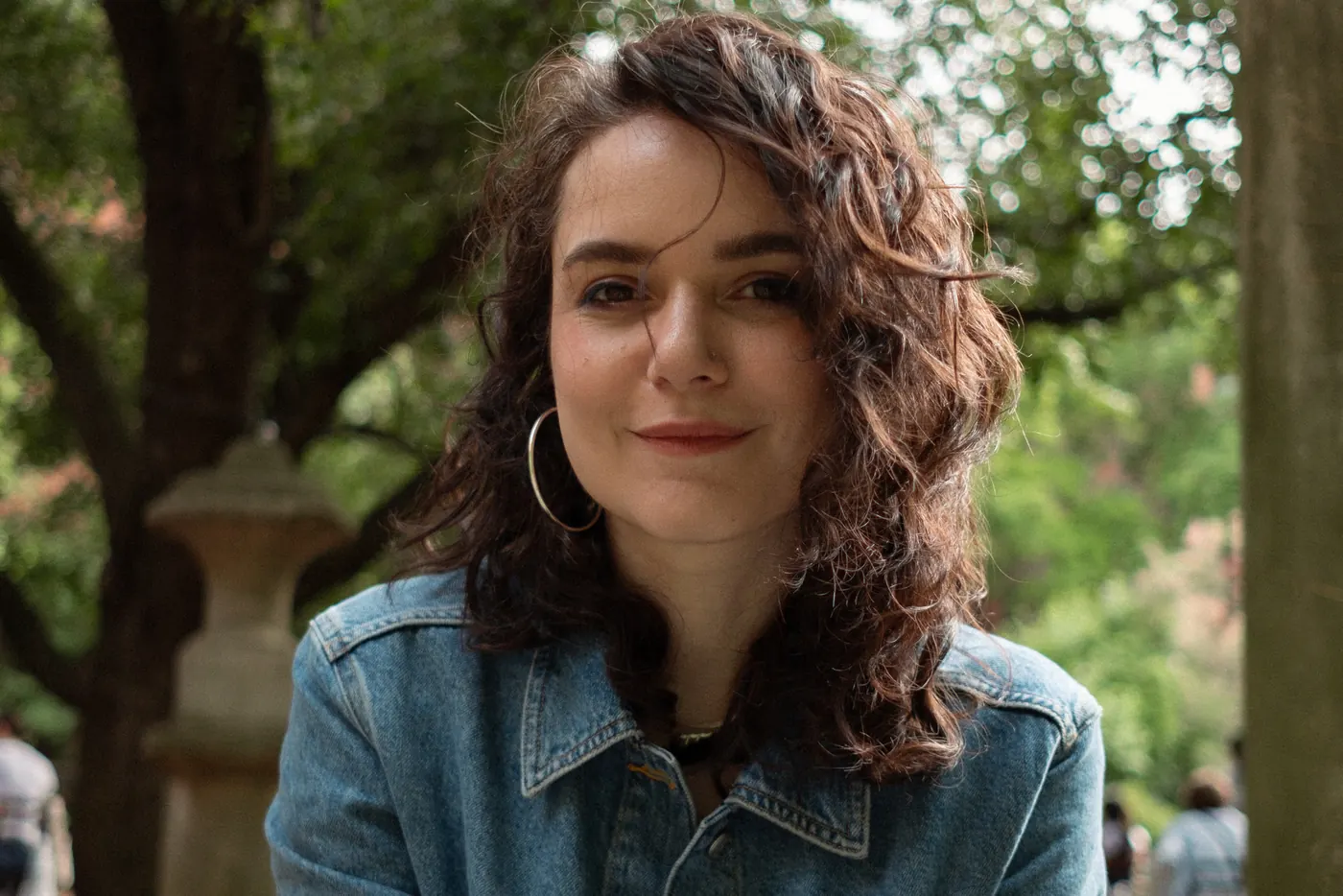 Portrait of a woman with curly hair in a denim jacket, smiling in a park