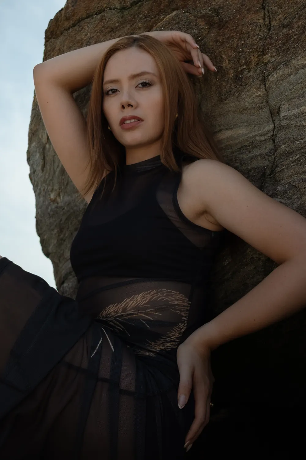 Red-haired woman leaning against a rock, arm raised