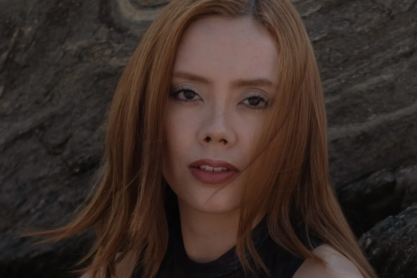 Close-up of a red-haired woman against a rock wall