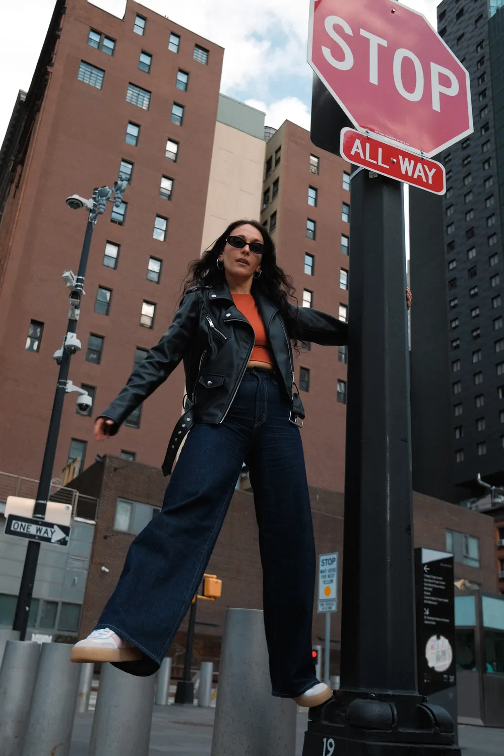 Woman in wide jeans swinging from a stop sign pole