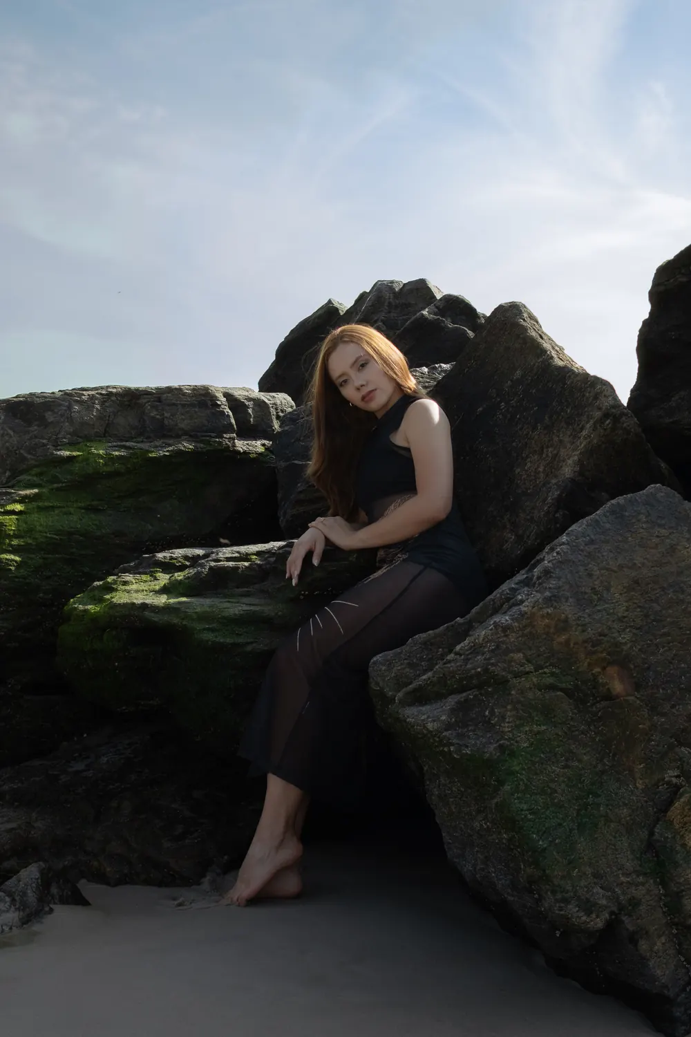 Red-haired woman sitting among beach rocks